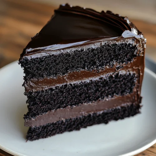 Slice of black velvet cake with dark, glossy ganache on a plate